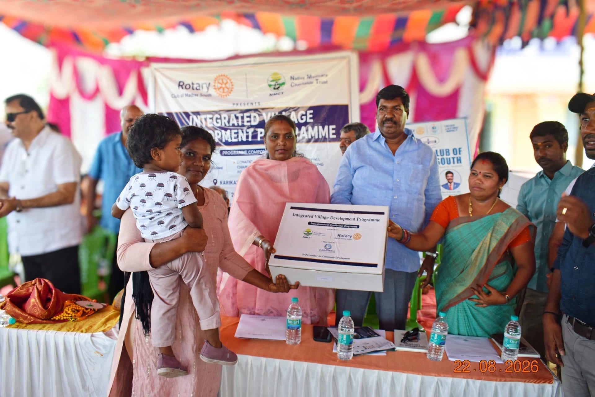 A mother holding her child receives an Integrated Village Development Programme kit from guests