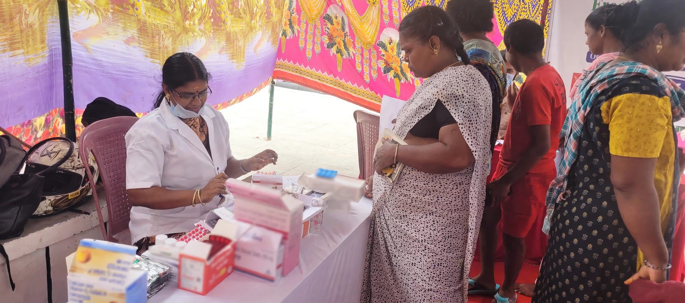A doctor at a medicines table attends to women at a Sanjeevi community medical camp