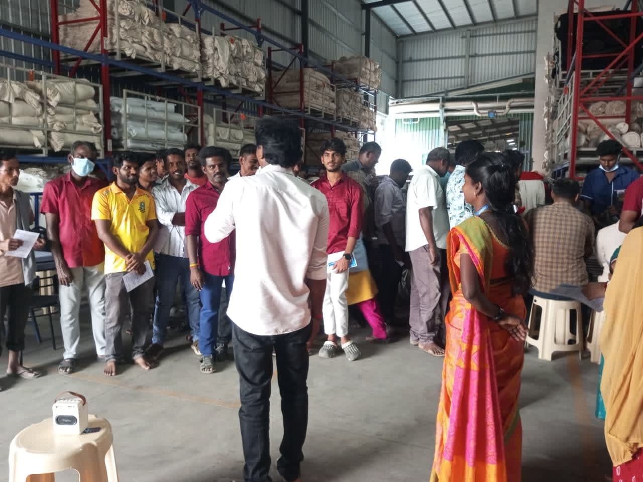 An NMCT outreach worker speaking with a group of migrant workers inside a factory