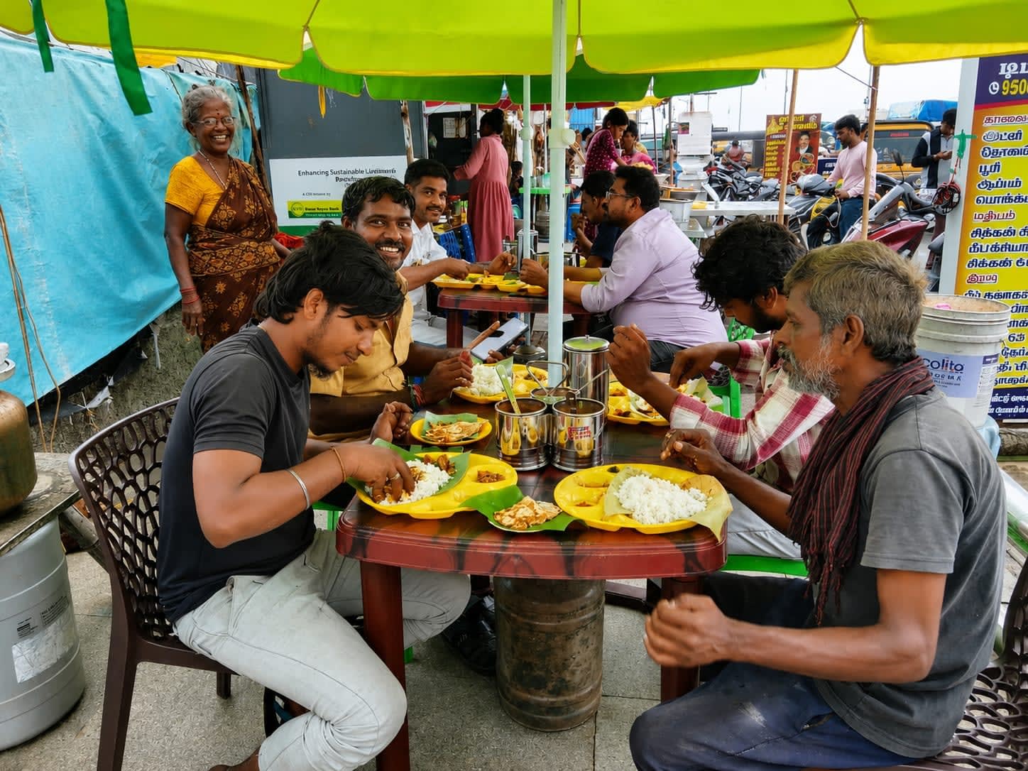 Customers eating at a street food stall under a green umbrella in Pattinapakkam